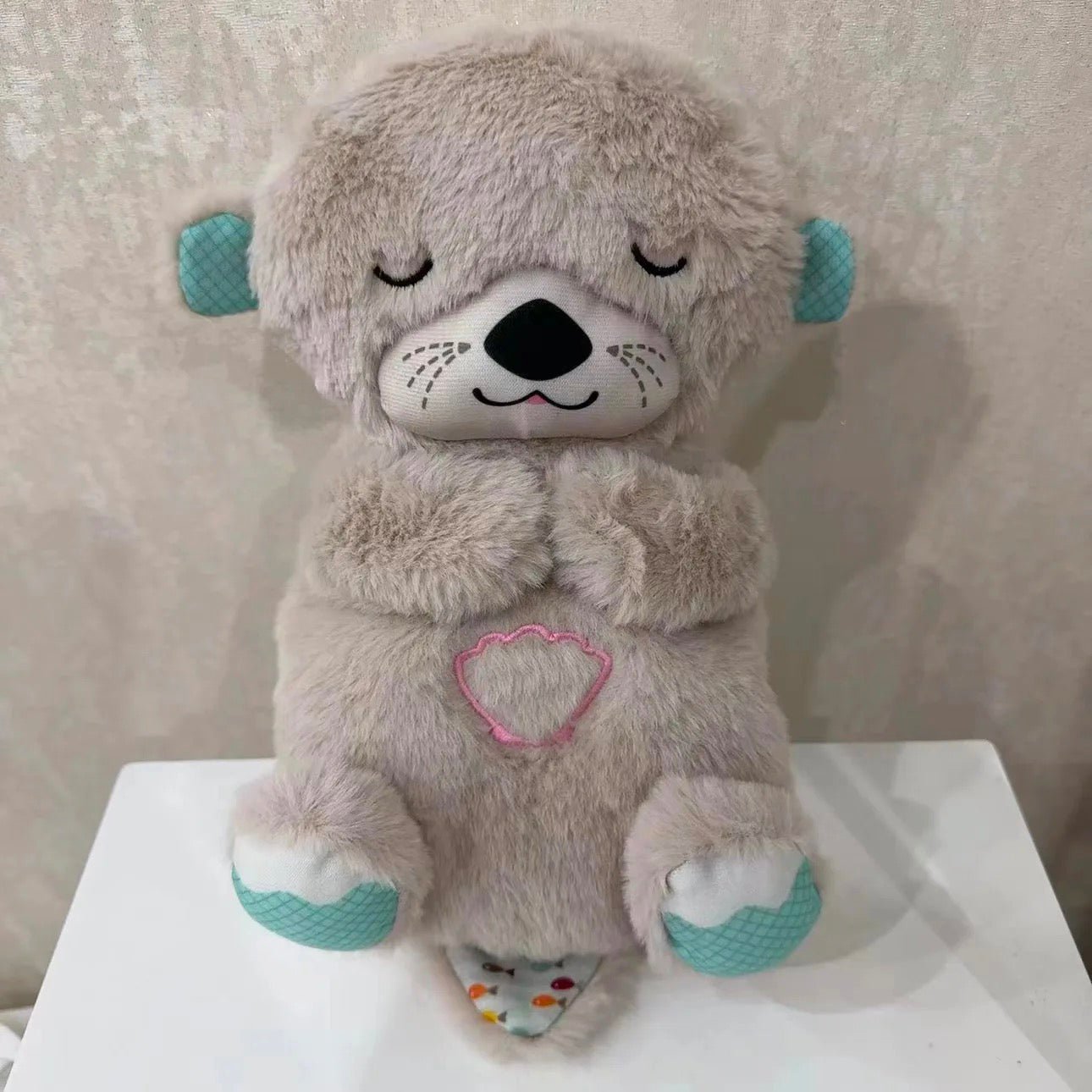 Gray plush bear sleep aid with closed eyes and pink outlined heart patch on chest