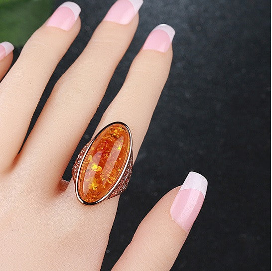 Oval amber statement ring worn on hand, yellow-orange resin center and dark filigree sides