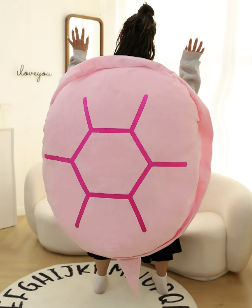 Pink plush turtle-shell pillow with magenta hexagon pattern, worn as a neck and shoulder wrap