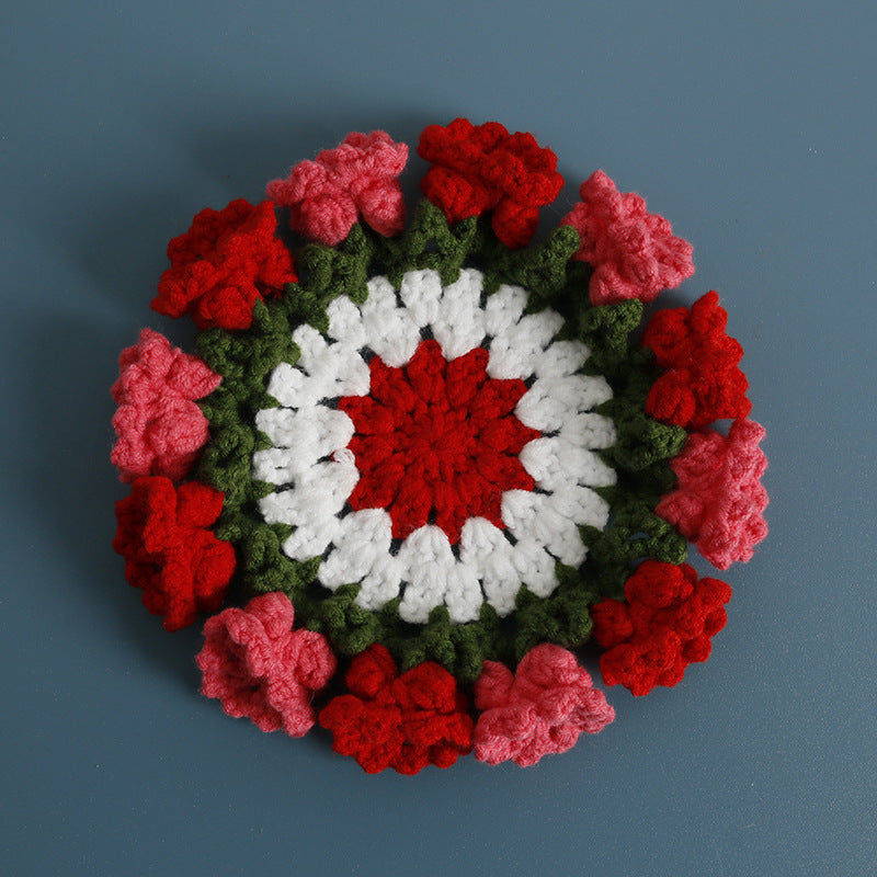 Crochet coaster with white center, red roselets, and dark green leafy border