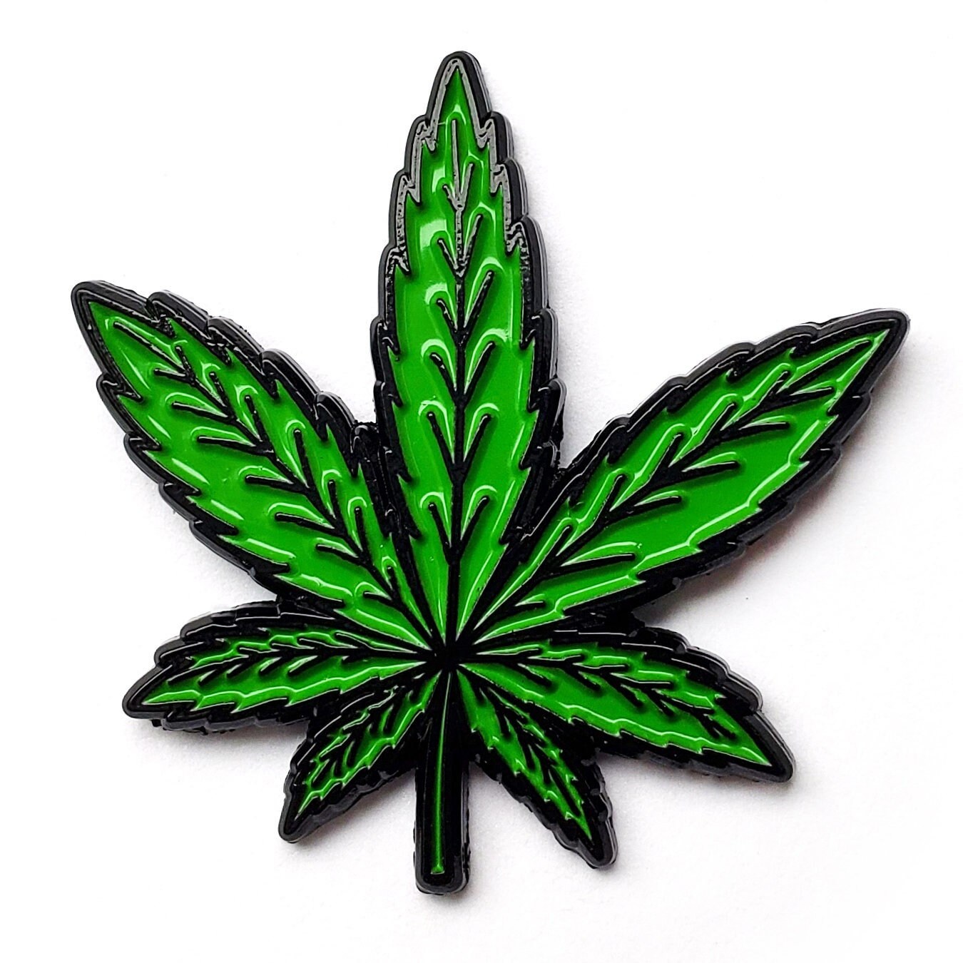 Green cannabis leaf soft enamel fridge magnet on dark metal backing