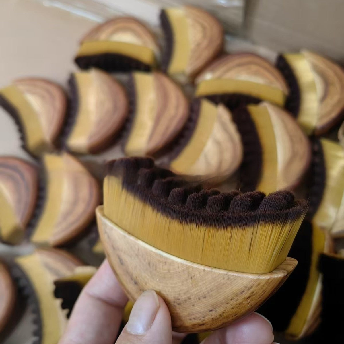 Wooden facial massage brush in hand with dense brown ridged bristles