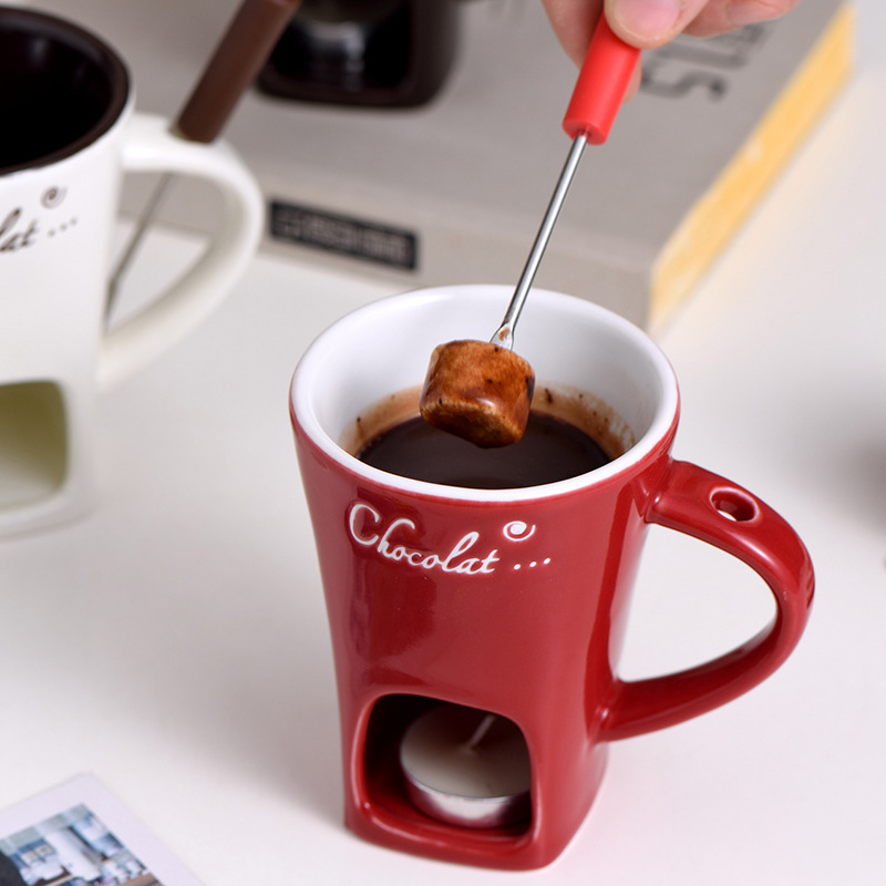 Red mini fondue mug with handle and metal fork stirring melted chocolate