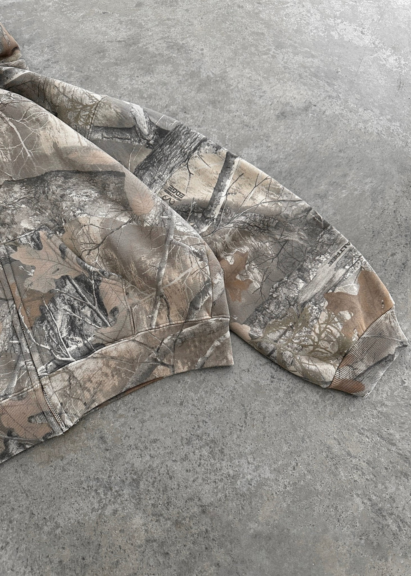 Camouflage hoodie sleeves, tree-branch print in gray and tan tones