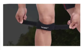 Black knee massager strap with control pad being fastened around a knee