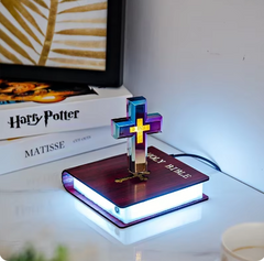 Decorative cross on a book with LED lighting, placed on a surface with books in the background.