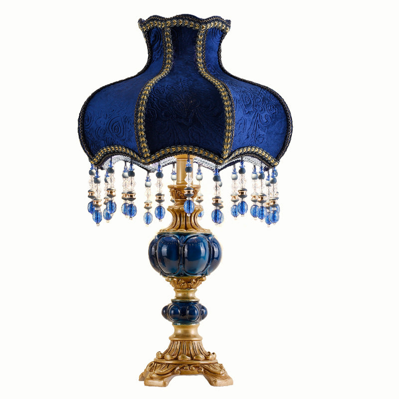 Blue fabric table lamp with gold trim, crystal bead fringe, and decorative gold base pedestal