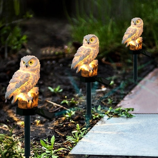 Three white owl garden lamps on black stakes with warm light glowing