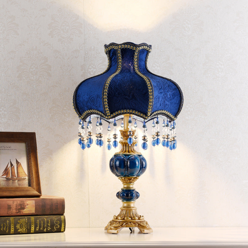 Lit blue table lamp with fabric shade, gold trim, and crystal drop fringe over a gold base