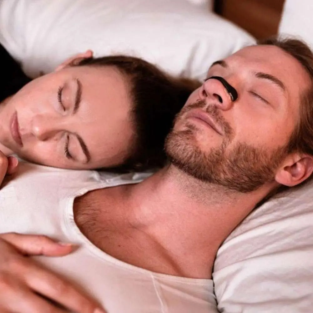 Two people sleeping; man in front wears a black nasal dilator strip