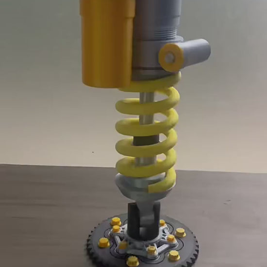 A model of a mechanical spring assembly with yellow coils and gray cylindrical components.