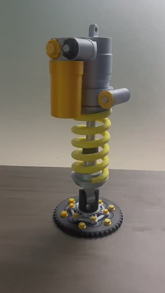 A model of a mechanical spring assembly with yellow coils and gray cylindrical components.